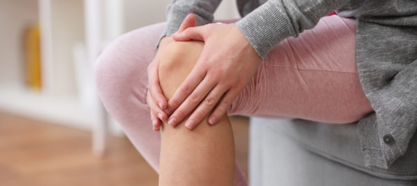 Young woman suffering from pain in knee, close up